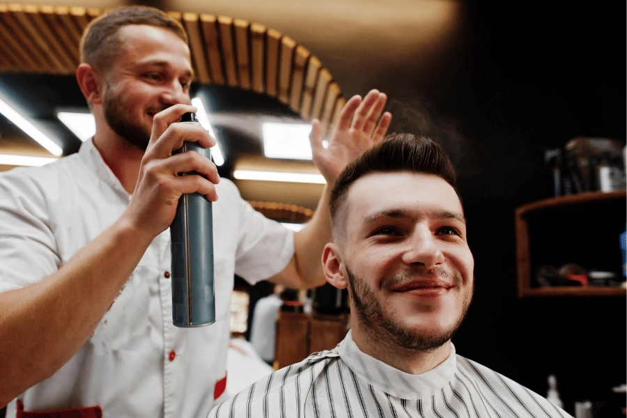 Barber spraying hairspray on customer