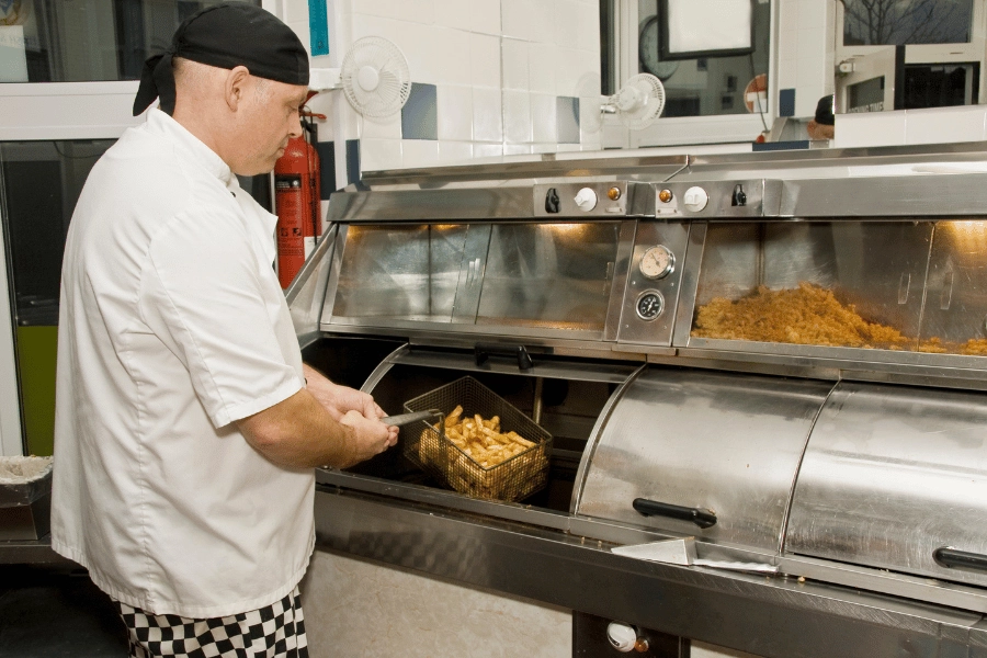 Chip shop worker putting chips in a deep fat fryer